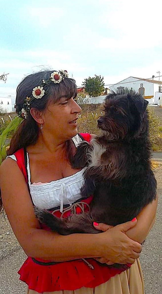 Woman in traditional dress holding her small black terrier Cookie, sharing a tender gaze outdoors.